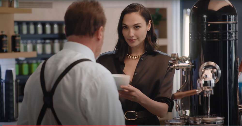 Gal Gadot serving Arnold Schwarzenegger a cup of Caffe Latte from a Bezzera Verticale Black Eagle 2 Group Coffee Machine